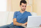 Casual peaceful man sitting on couch using laptop