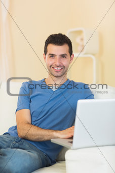 Casual cheerful man sitting on couch using laptop