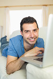 Casual happy man sitting on couch using laptop looking at camera