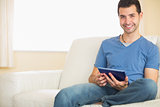Casual smiling man using tablet sitting on couch