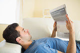 Casual peaceful man lying on couch reading  newspaper