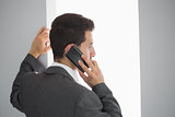 Rear view of businessman standing in front of window phoning