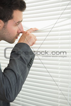 Handsome serious businessman spying through roller blind
