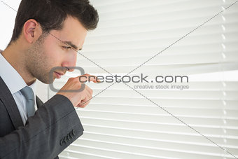 Handsome unsmiling businessman spying through roller blind