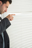 Handsome frowning businessman spying through roller blind