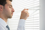 Attractive frowning businessman spying through roller blind