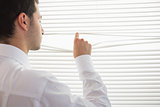 Rear view of handsome businessman spying through roller blind