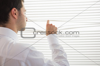 Rear view of handsome businessman spying through roller blind