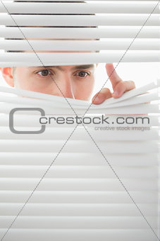 Serious male eyes spying through roller blind