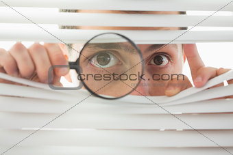 Male eyes spying through roller blind with loupe