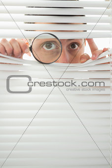 Male eyes spying through roller blind with magnifier