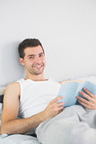Handsome smiling man reading book in his bed