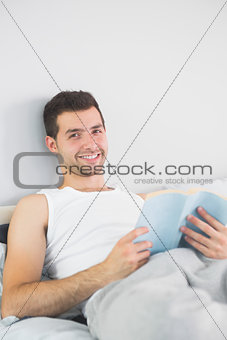 Handsome smiling man reading book in his bed
