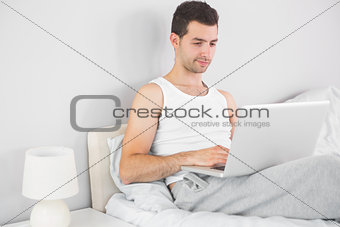 Handsome smiling man using laptop in his bed