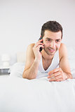 Smiling handsome man lying in bed phoning