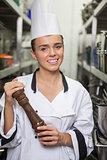 Young cheerful chef holding pepper mill between shelves
