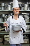 Young smiling chef holding pot in front of shelf