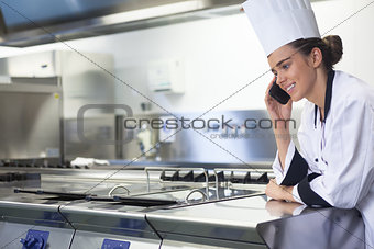 Young smiling chef standing next to work surface phoning