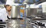 Young pretty chef standing next to work surface phoning