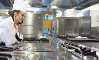 Young pretty chef standing next to work surface phoning