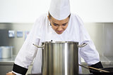 Young pretty chef looking into saucepan