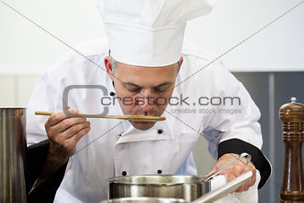 Focused head chef tasting sauce with wooden spoon