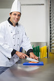 Smiling chef cutting raw salmon with knife on blue cutting board