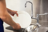 Kitchen porter cleaning white plates in sink