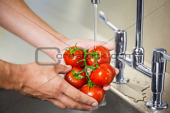 Kitchen porter washing tomatoes under running tap