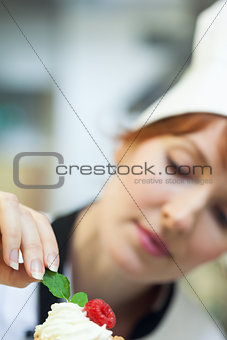 Concentrating head chef putting mint leaf on little cake