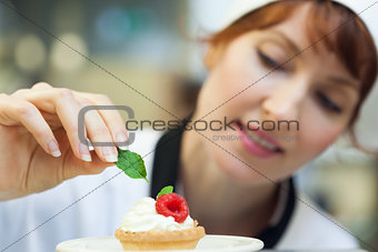Happy head chef putting mint leaf on little cake