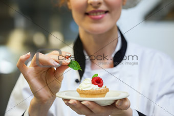 Happy head chef putting mint leaf on little cake on plate