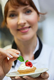 Pretty head chef putting mint leaf on little cake on plate