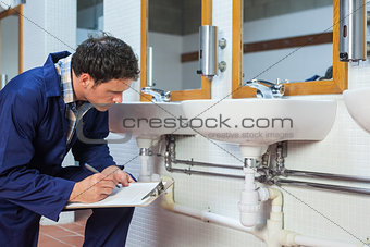 Handsome plumber looking at sink holding clipboard
