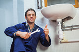 Handsome plumber sitting next to sink showing thumb up