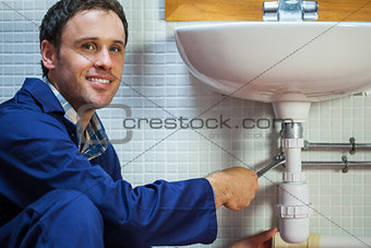 Handsome smiling plumber repairing sink