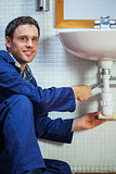 Handsome cheerful plumber repairing sink