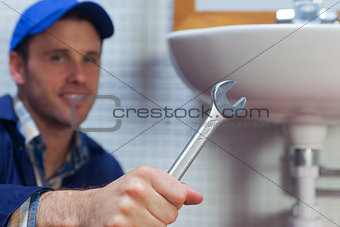Handsome cheerful plumber showing wrench