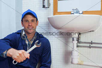Smiling plumber holding wrench sitting next to sink