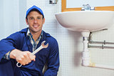 Happy plumber holding wrench sitting next to sink