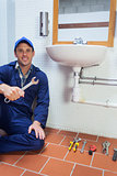 Cheerful plumber holding wrench sitting next to sink
