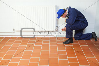 Handyman in blue boiler suit repairing a radiator