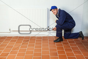 Handyman in blue boiler suit repairing a radiator smiling at camera