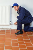 Happy handyman in blue coveralls repairing a radiator