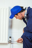 Serious handyman in blue coveralls repairing a radiator
