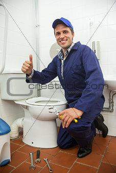Plumber kneeling next to toilet showing thumb up