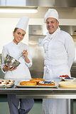 Smiling chef holding whisk while being watched by head chef