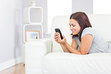 Content casual woman working with her smartphone while lying on her couch