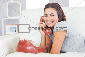Amused young woman using a red dial phone