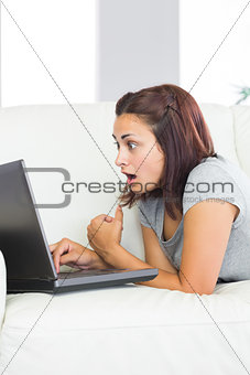 Brunette young woman using her notebook lying taken aback in front of it